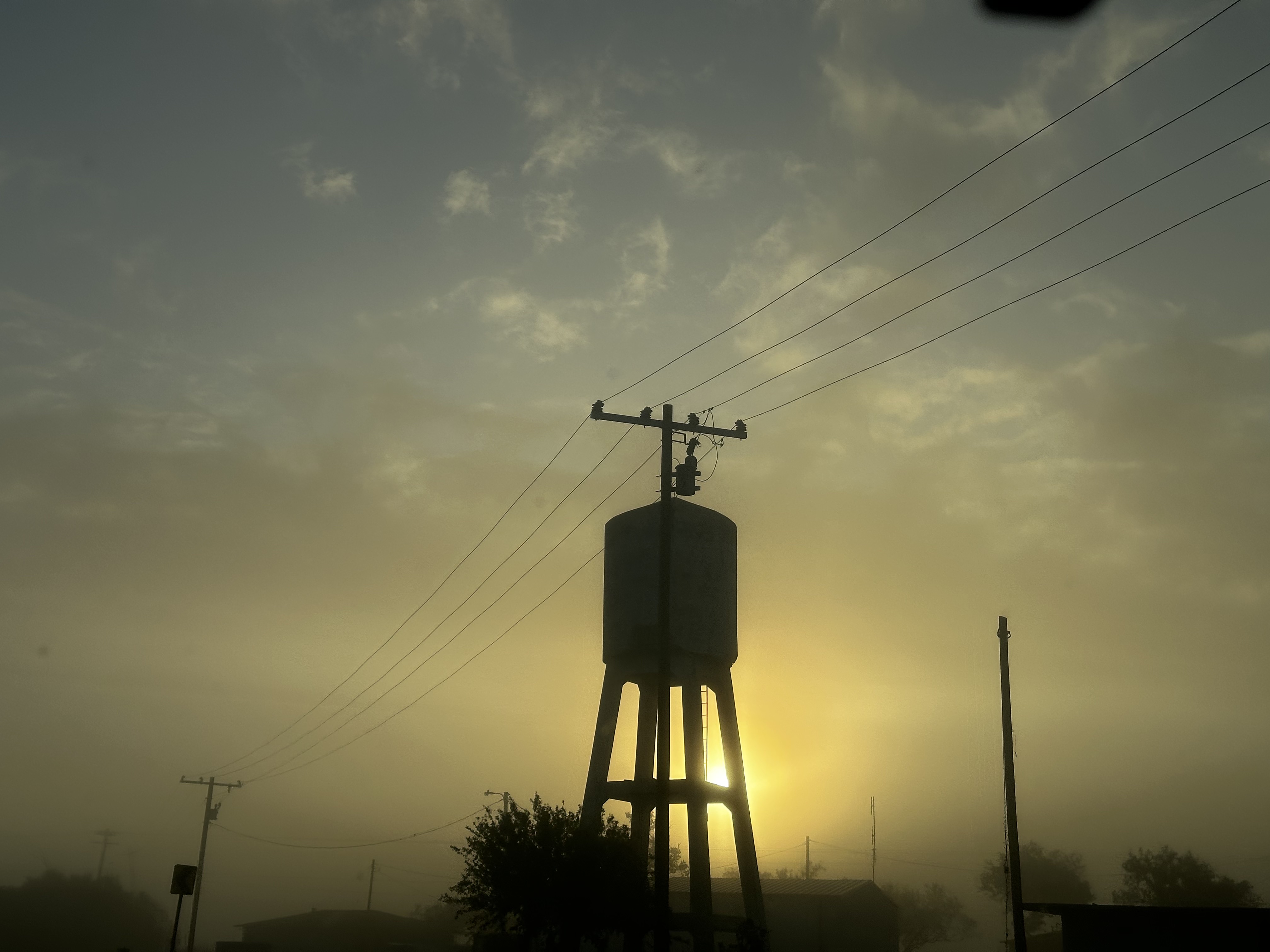 Water tower and utility lines silhouetted against the low sun